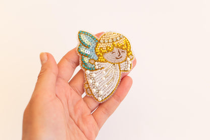 A hand holding a decorative beaded object resembling an angel or a similar figure.