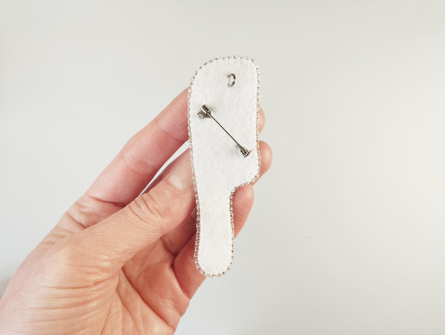 A hand holding a white pin cushion with a pin attached to it.