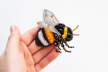a hand holding a beaded bee on a white background