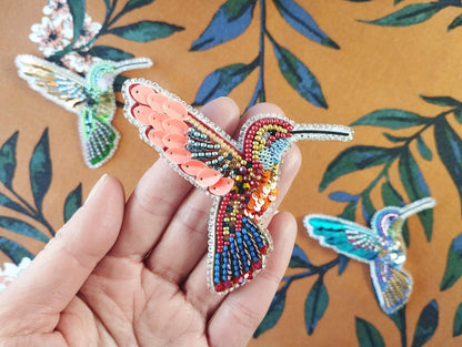 a hand holding a small beaded humming bird