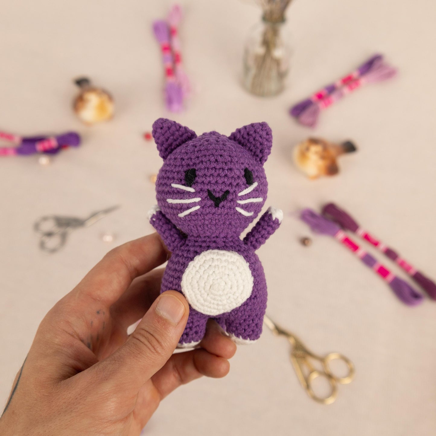 a hand holding a small crocheted purple cat