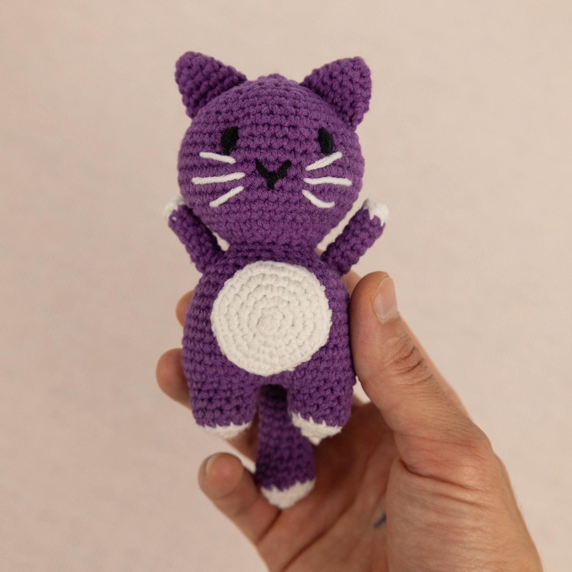 a hand holding a small crocheted purple cat