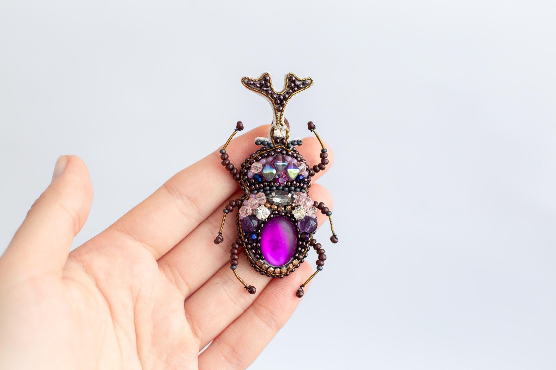 a hand holding a purple and black insect brooch