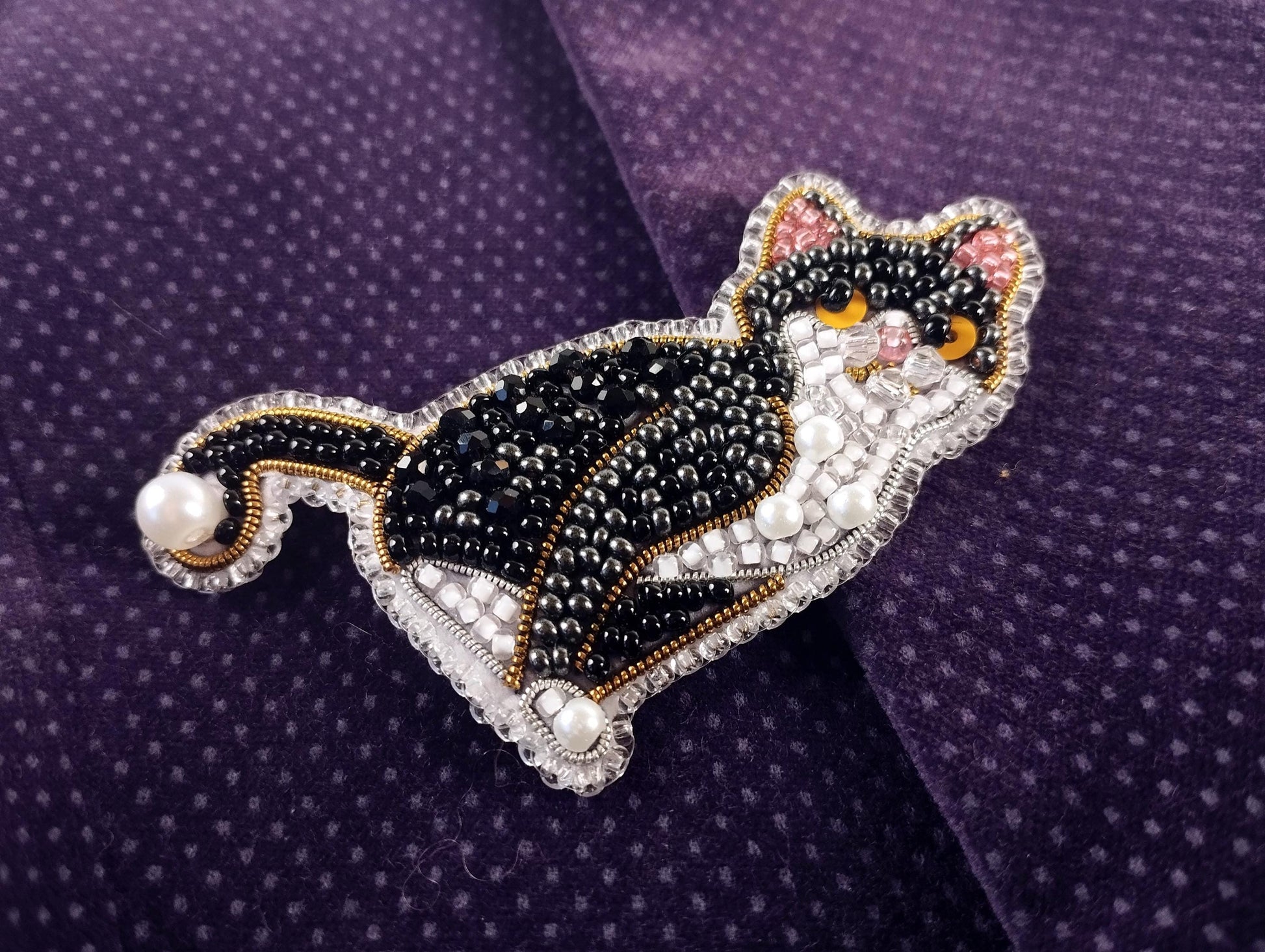 A decorative cat brooch made of beads and pearls, featuring a black and white color scheme with a detailed design.