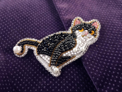 A decorative cat brooch made of beads and pearls, featuring a black and white color scheme with a detailed design.