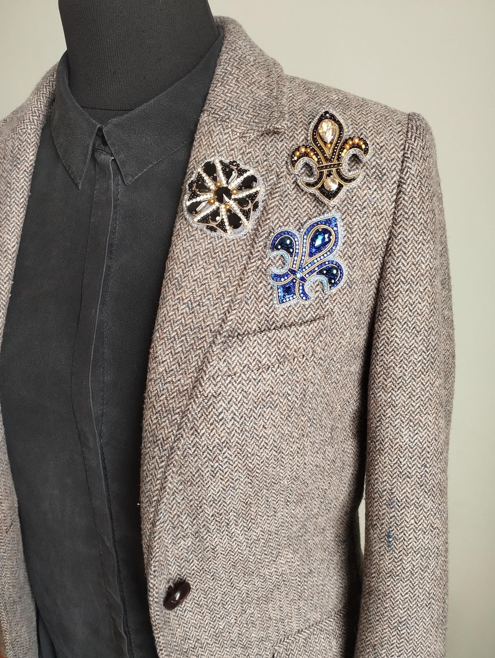 A mannequin wearing a gray tweed blazer with three decorative buttons on the left side.