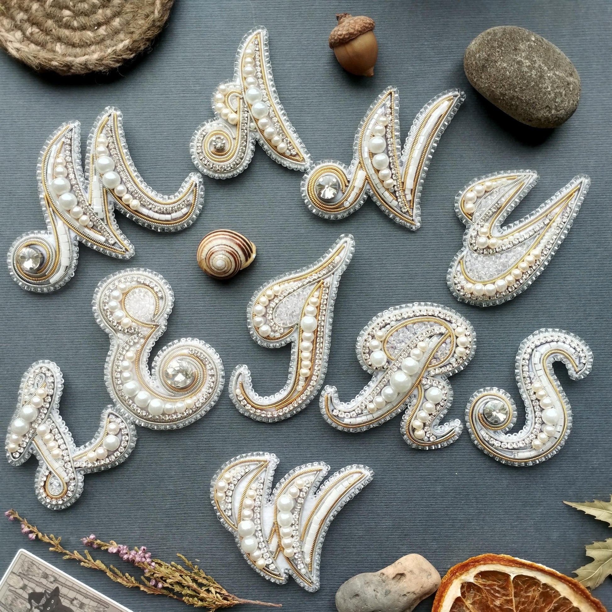 a collection of decorative elements, including beads, stones, and a small acorn, arranged to spell out the word "MAY".