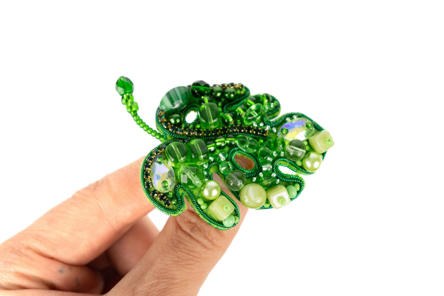a hand holding a green brooch with pearls