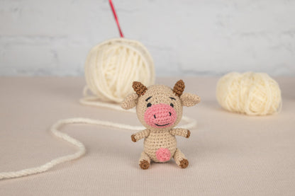 a small stuffed cow sitting next to a ball of yarn