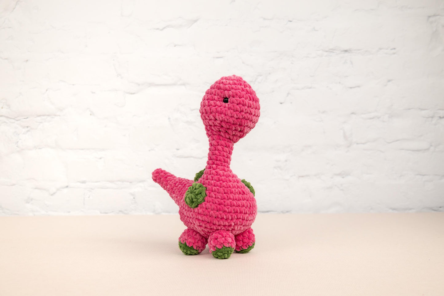 a crocheted pink dinosaur sitting on a table