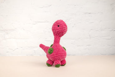 a crocheted pink dinosaur sitting on a table