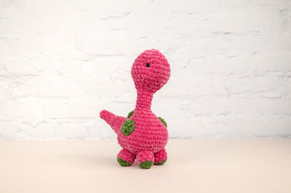 a crocheted pink dinosaur sitting on a table