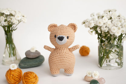 a crocheted teddy bear standing next to a vase of flowers