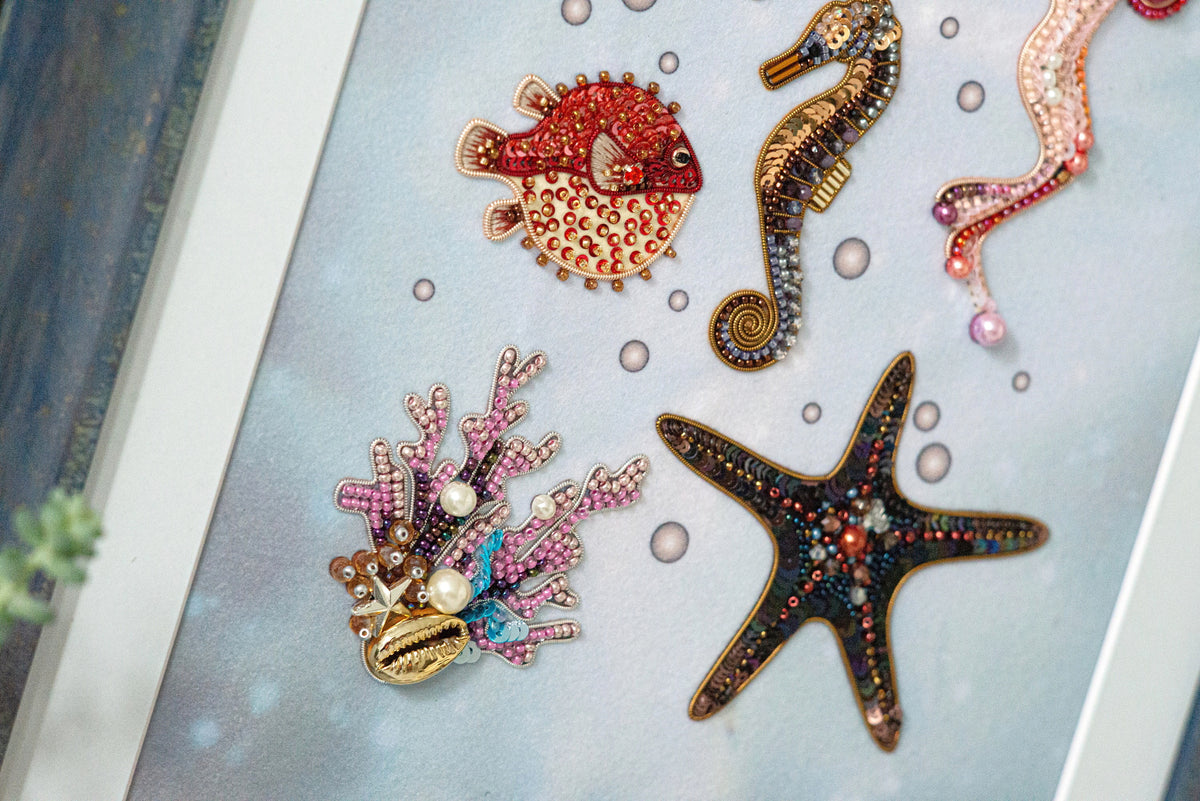 a collection of colorful and intricately designed sea-themed ornaments, including a red fish, a pink and purple coral, a black starfish, and a pink and purple sea shell.
