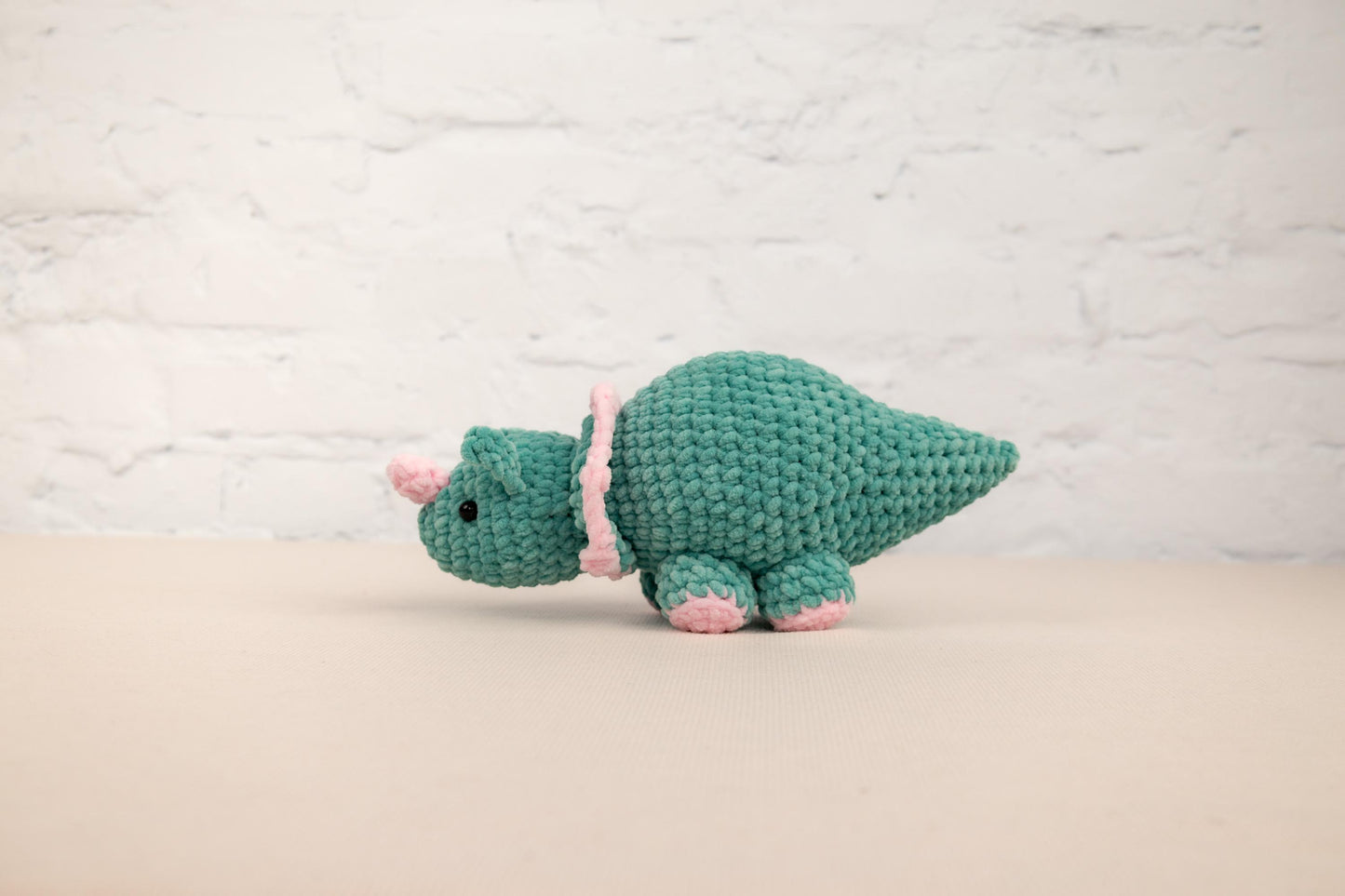 a green crocheted stuffed animal with a pink ribbon