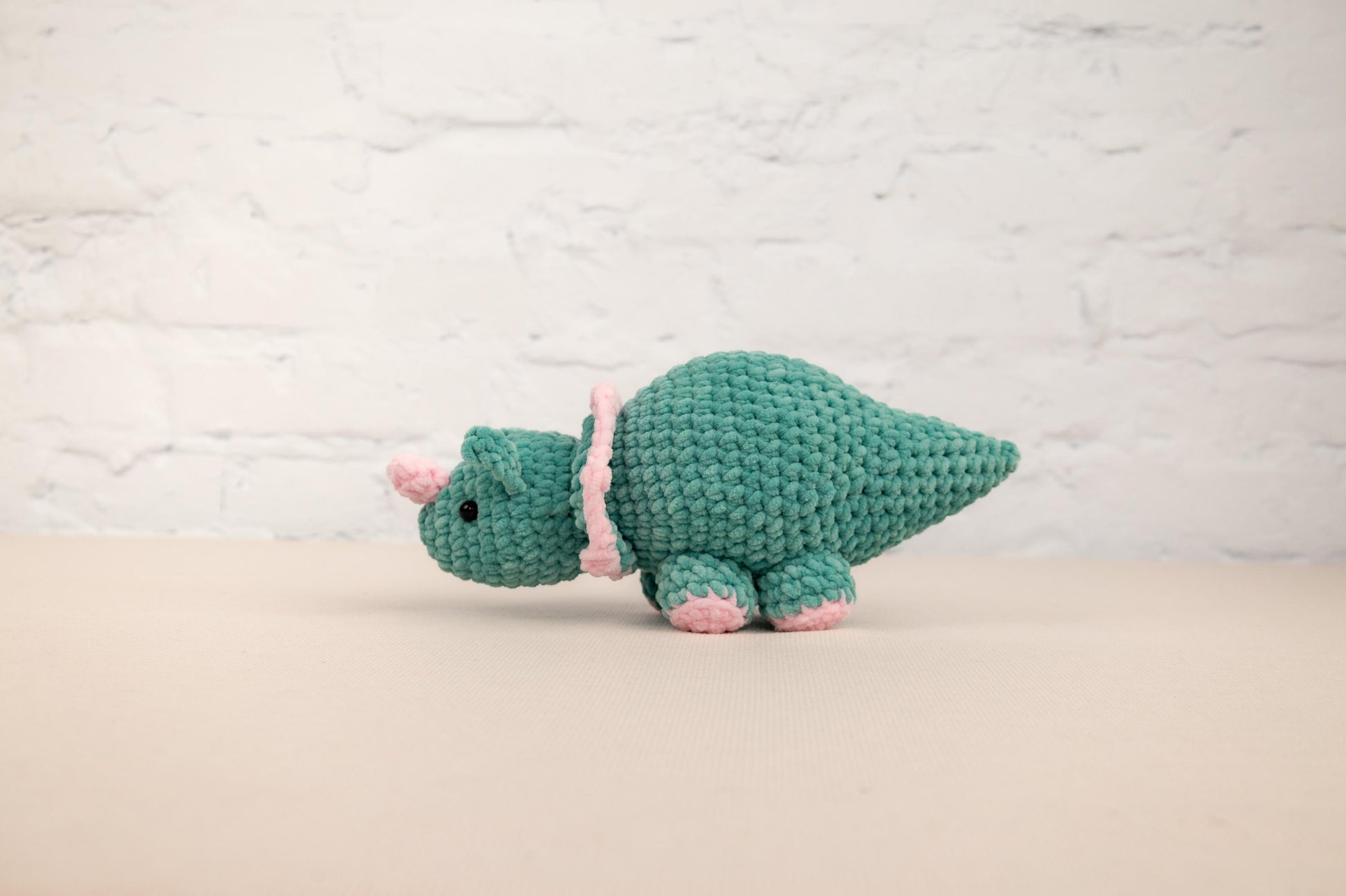 a green crocheted stuffed animal with a pink ribbon