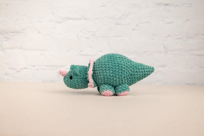 a green crocheted stuffed animal with a pink ribbon
