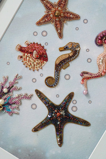a collection of colorful, intricately designed sea-themed ornaments, including a starfish, a fish, and a seahorse, all adorned with beading and other embellishments.