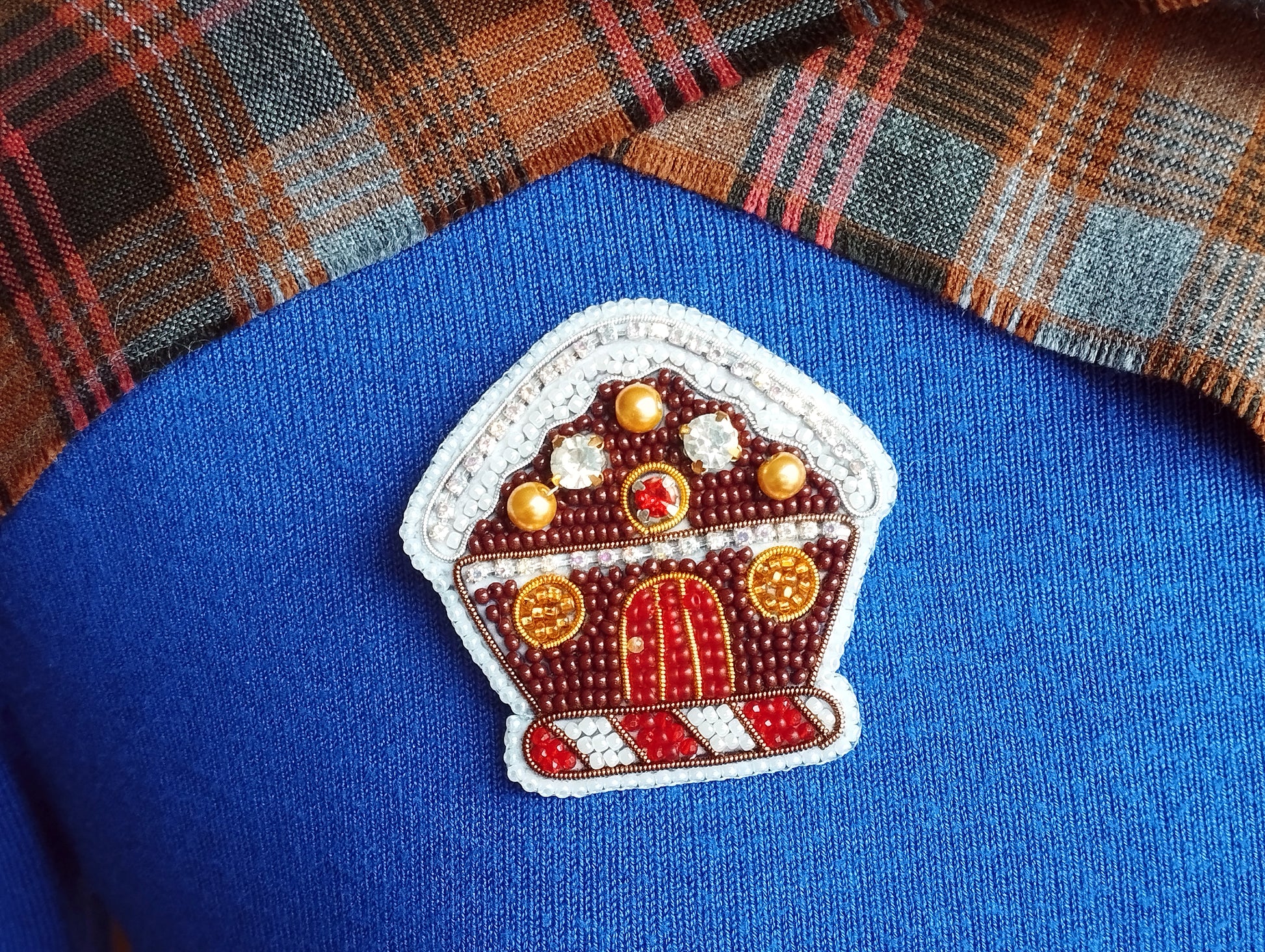 A close-up of a blue sweater with a decorative button in the shape of a gingerbread house.