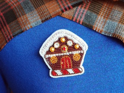 A close-up of a blue sweater with a decorative button in the shape of a gingerbread house.
