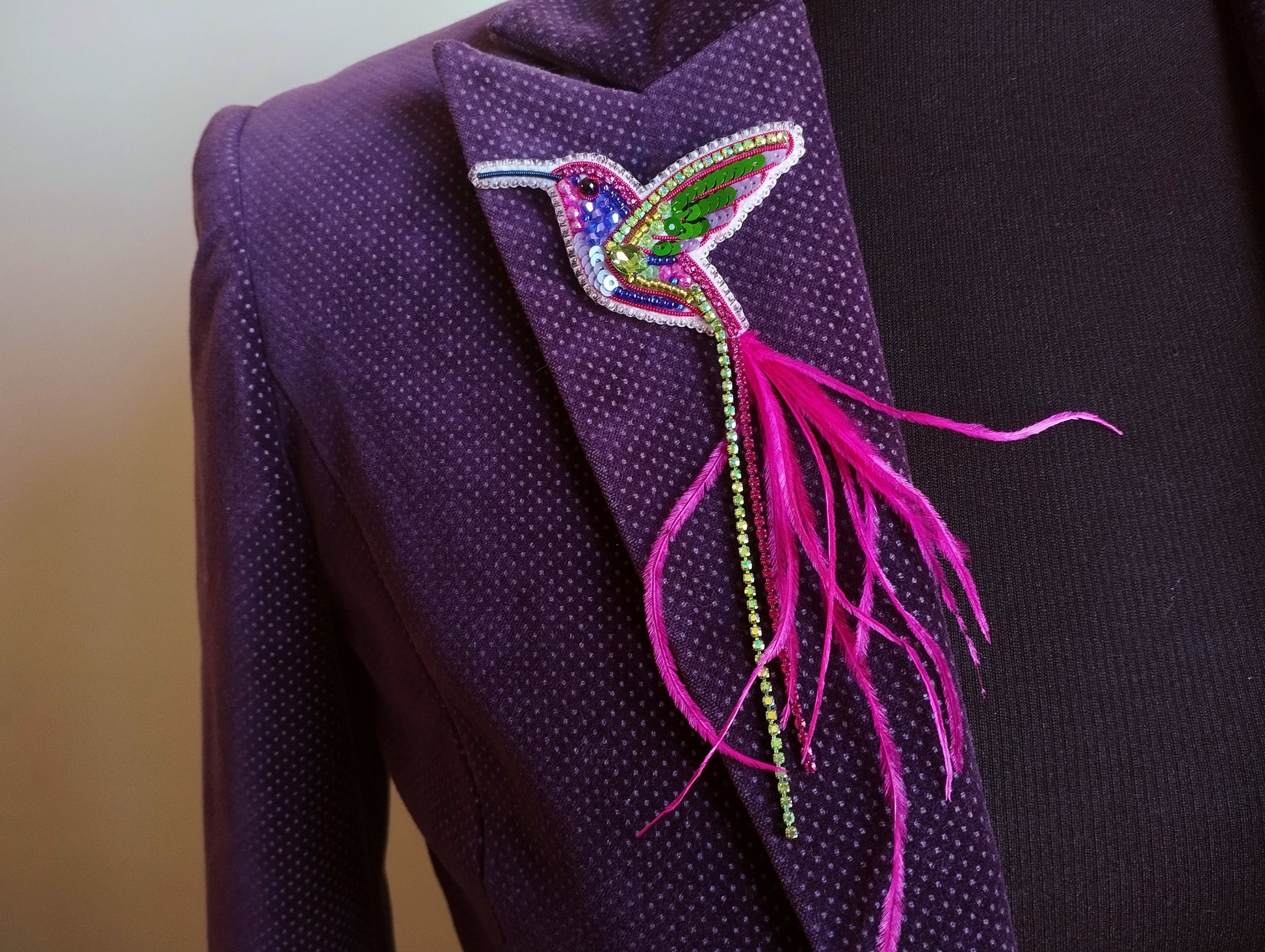 A close-up view of a purple jacket with a colorful, beaded bird brooch on the lapel.