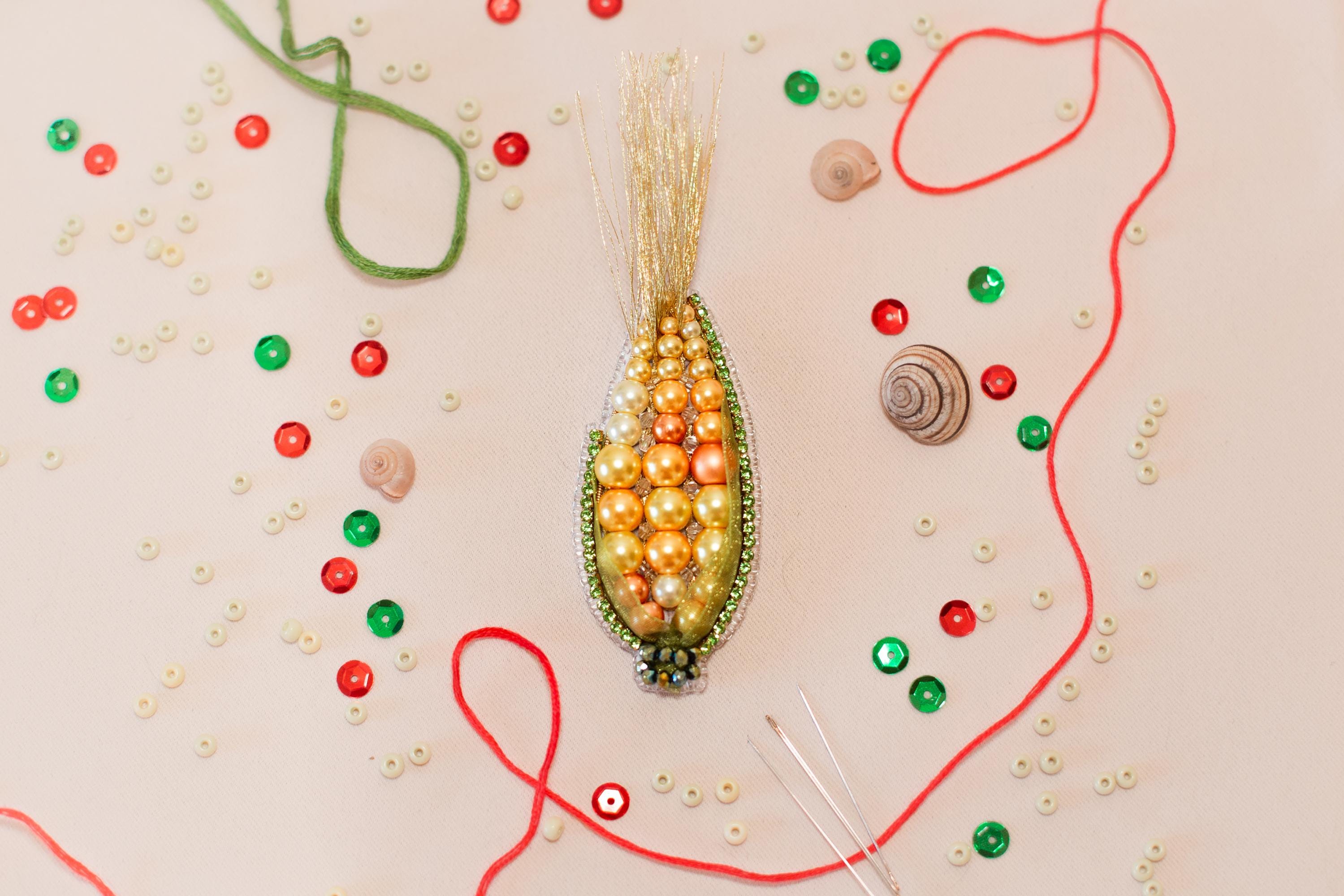 a close-up view of a colorful beaded corn cob, surrounded by various craft supplies such as beads, strings, and other embellishments.