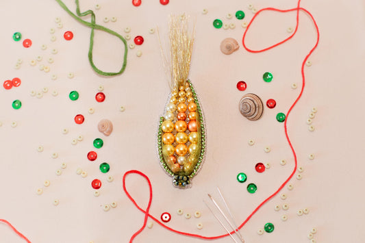 a close-up view of a colorful beaded corn cob, surrounded by various craft supplies such as beads, strings, and other embellishments.