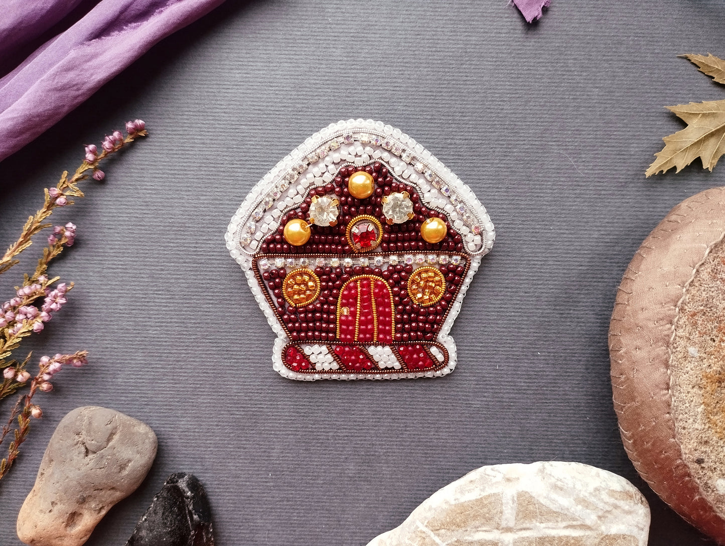 a decorative piece resembling a gingerbread house, surrounded by various natural elements such as leaves, rocks, and a purple fabric.