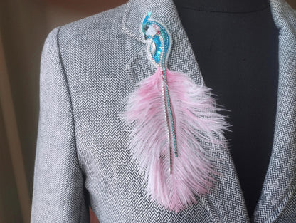 A close-up of a gray tweed jacket with a pink feather pin on the lapel.