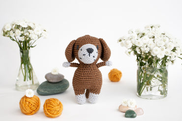 a crocheted dog standing next to a vase of flowers