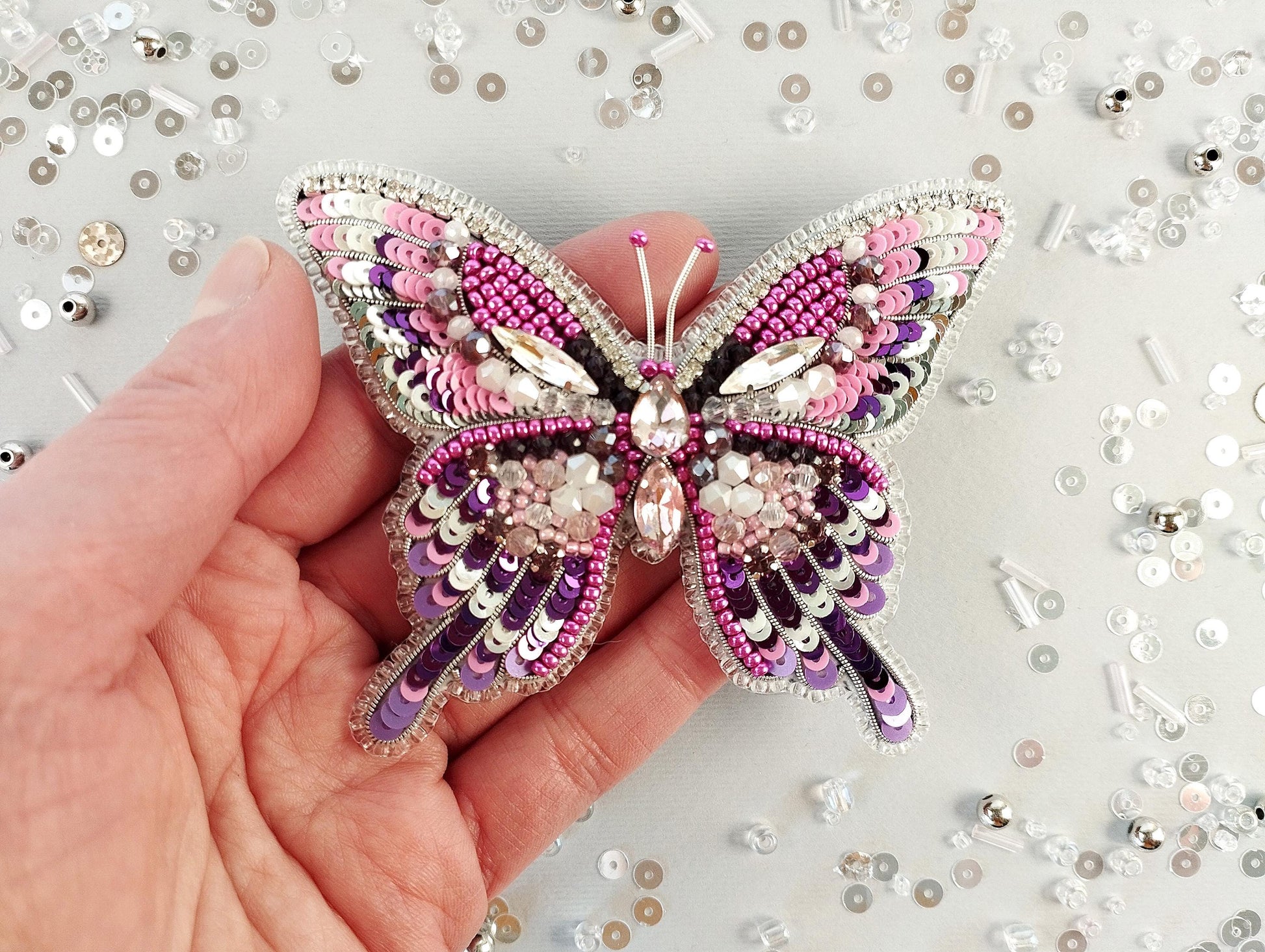 a hand holding a pink and purple butterfly brooch