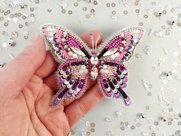 a hand holding a pink and purple butterfly brooch
