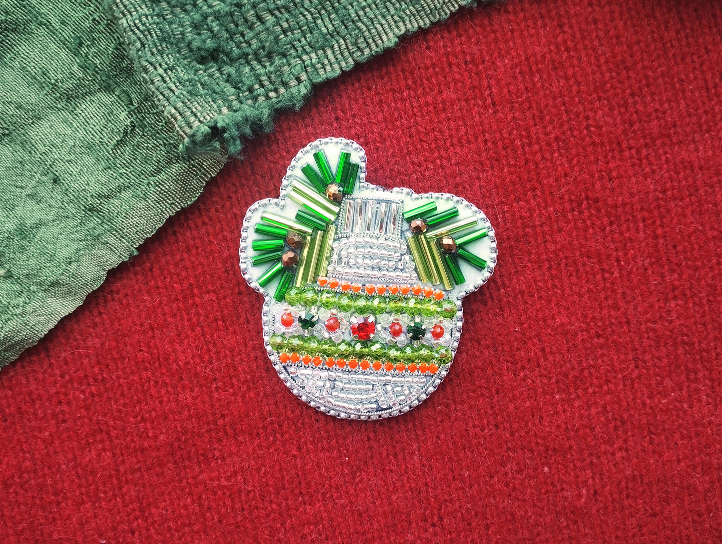 A decorative button or brooch with a colorful, intricate design, featuring a combination of green, red, and white elements, is displayed on a red surface.