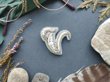 a decorative piece of jewelry, a brooch, surrounded by various natural elements such as leaves, feathers, and rocks.