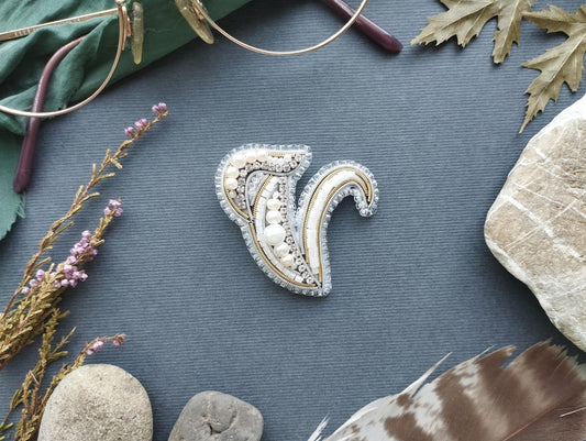 a decorative piece of jewelry, a brooch, surrounded by various natural elements such as leaves, feathers, and rocks.