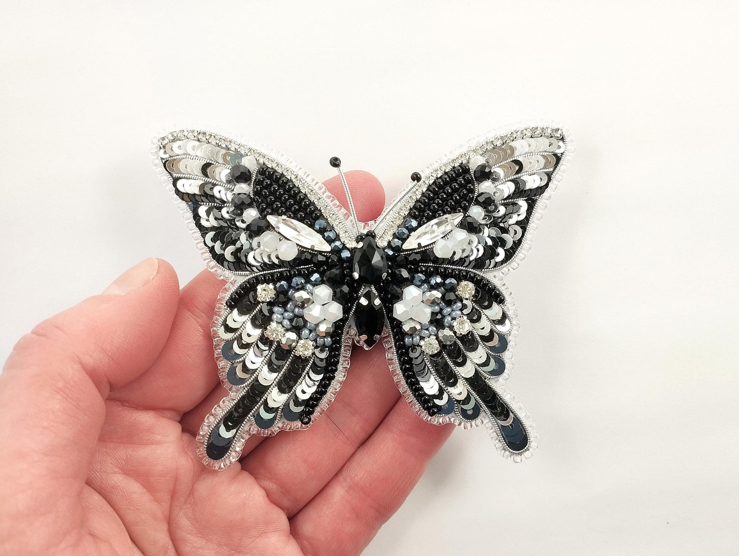 a hand holding a black and white butterfly brooch