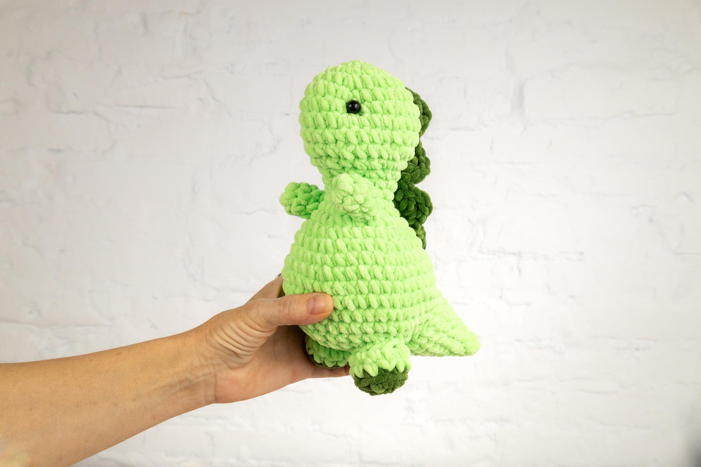 a hand holding a green crocheted stuffed animal