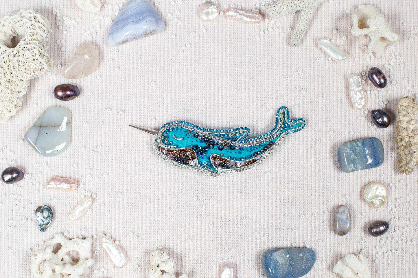 a blue and silver brooch with a whale design, surrounded by various natural elements such as pearls, seashells, and crystals.