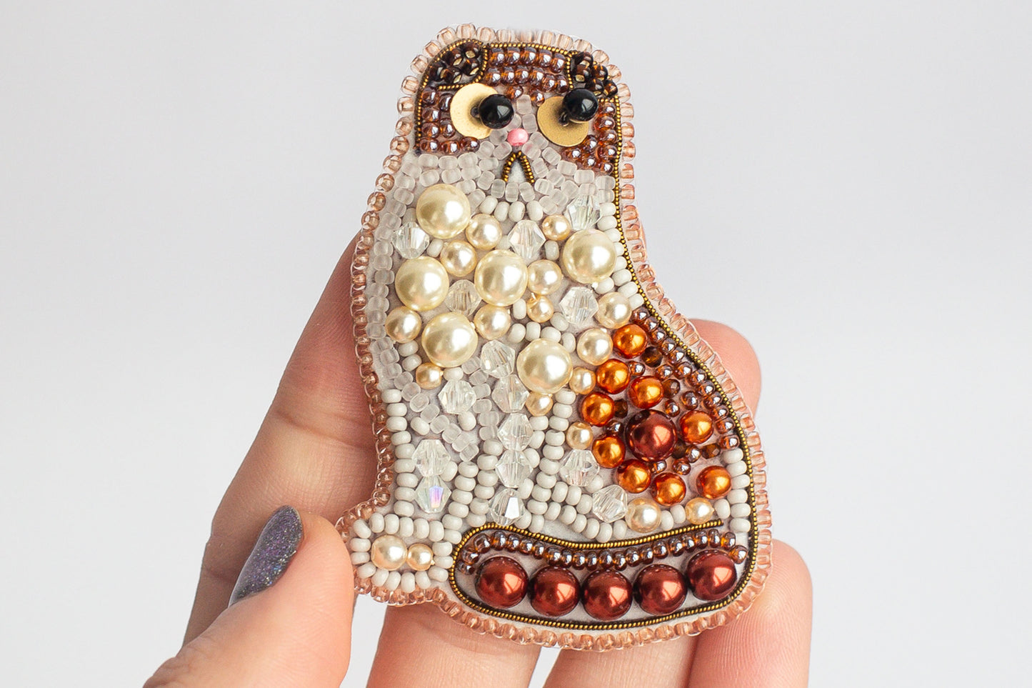 A hand holding a decorative cat-shaped object made of beads, pearls, and other embellishments.