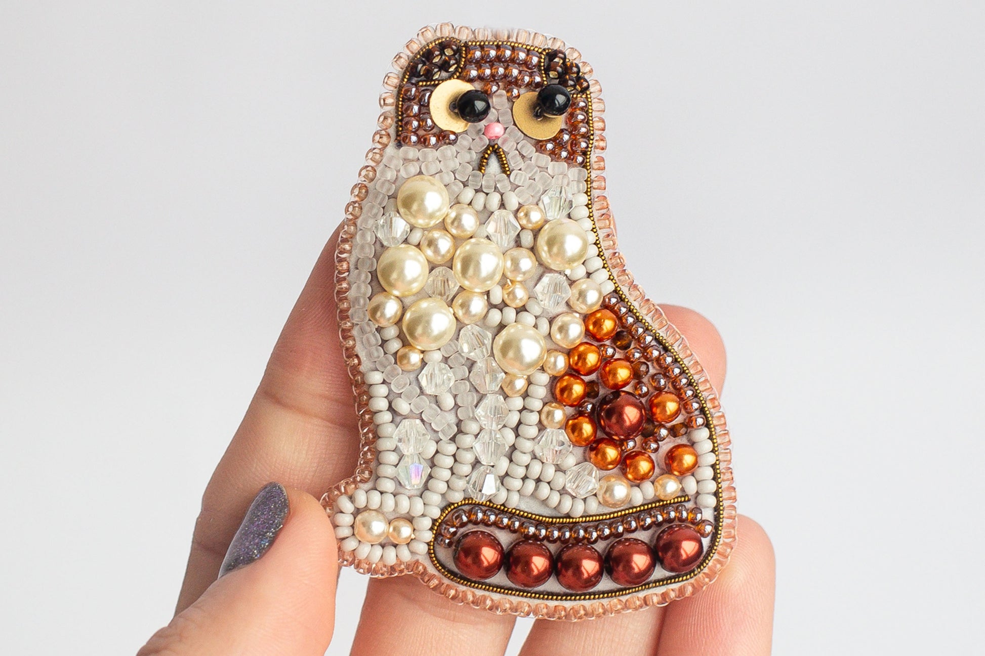 A hand holding a decorative cat-shaped object made of beads, pearls, and other embellishments.