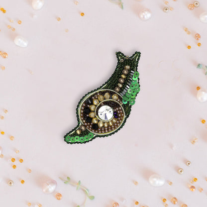 a green and brown brooch with a white background