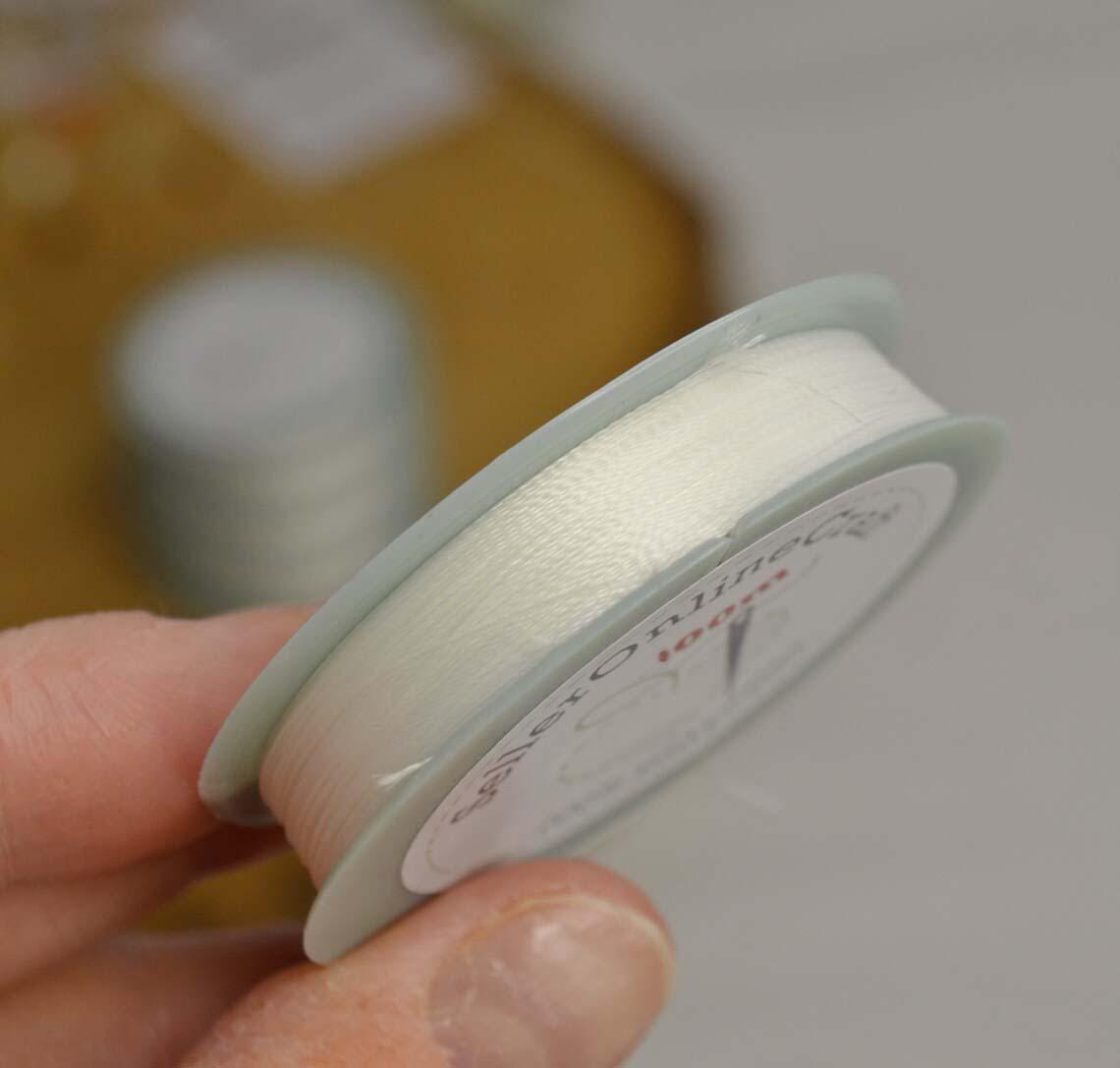 a hand holding a spool of white thread