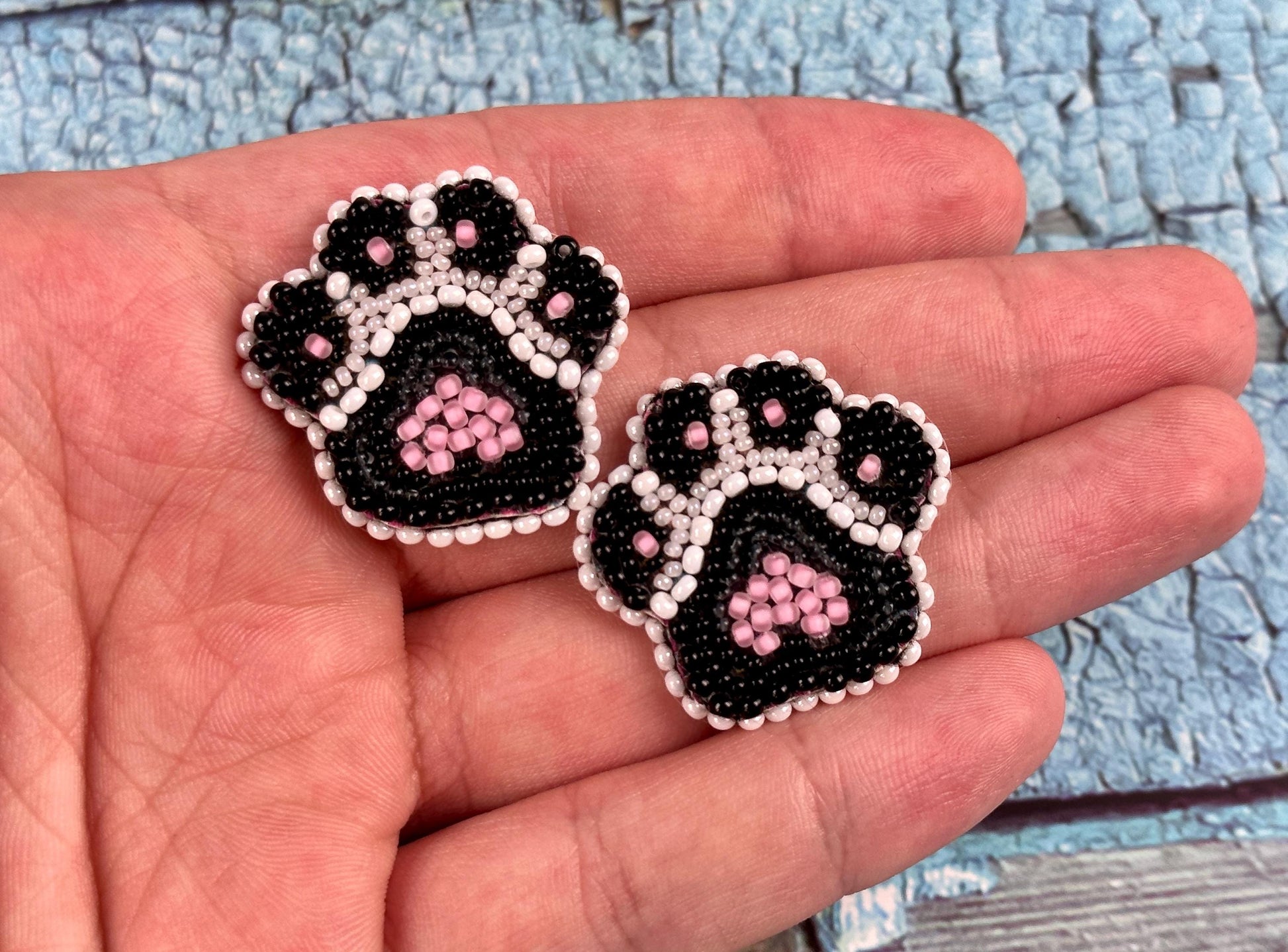 a hand holding a pair of black and white beaded dog paw earrings