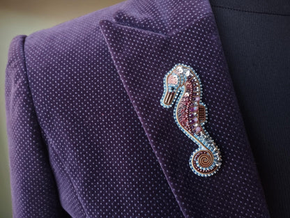 A close-up of a purple velvet jacket with a decorative seahorse brooch on the left side.