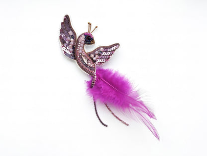 A decorative bird brooch with a feather and sequin design, featuring a purple and pink color scheme.