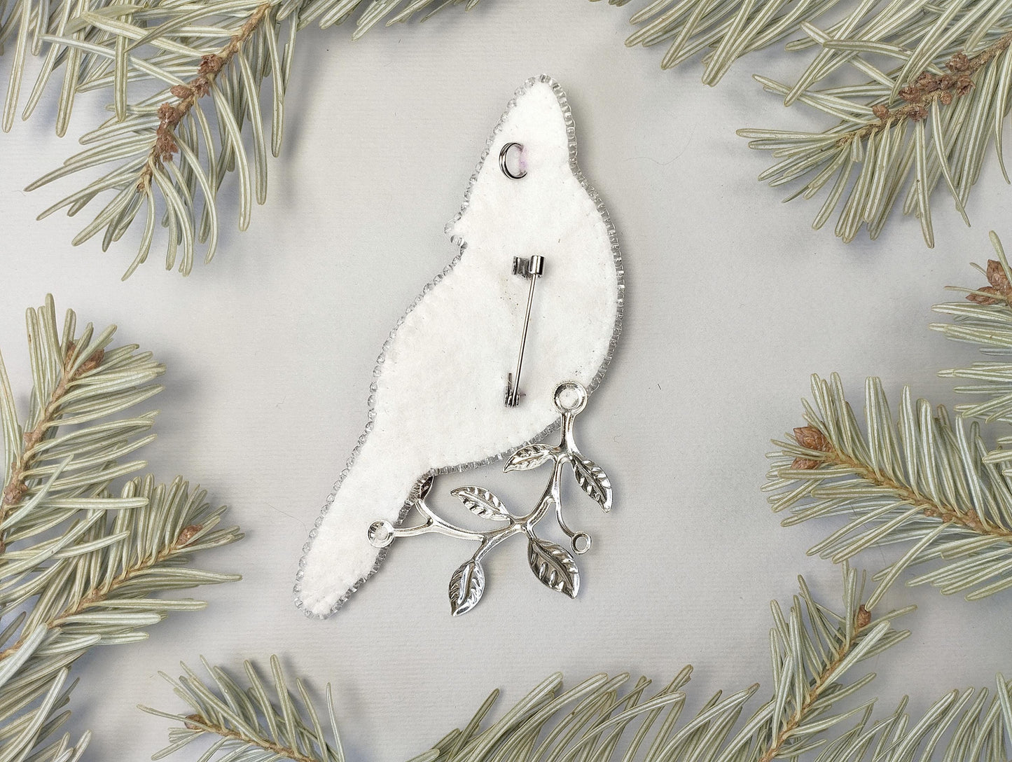 a white bird ornament hanging from a pine tree