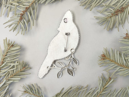a white bird ornament hanging from a pine tree