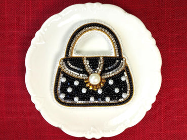 A white plate with a black and gold handbag-shaped design made of beads and pearls, placed on a red background.
