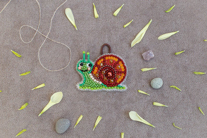a colorful bead necklace with a snail design, surrounded by various natural elements such as leaves, stones, and a string.