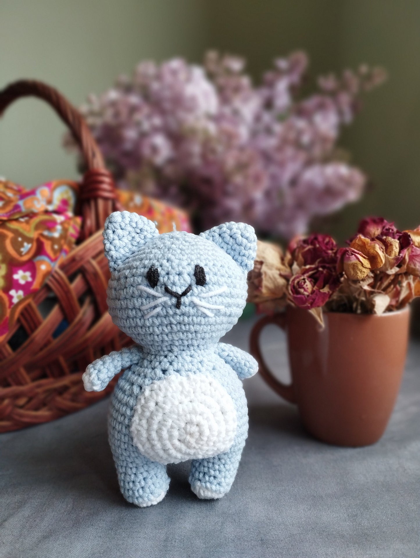 a crocheted cat sitting next to a basket of flowers